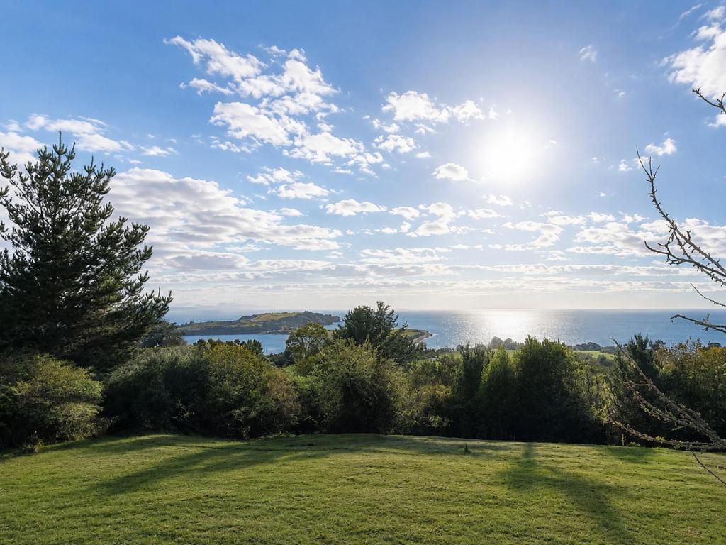 a view of the ocean from a field with trees at El Urco Chiloé - Cabaña Guapilacuy in Ancud