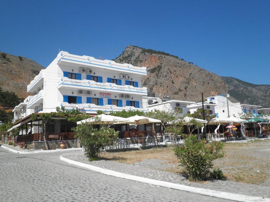 un grand bâtiment blanc avec des parasols dans une rue dans l'établissement Calypso, à Agía Rouméli