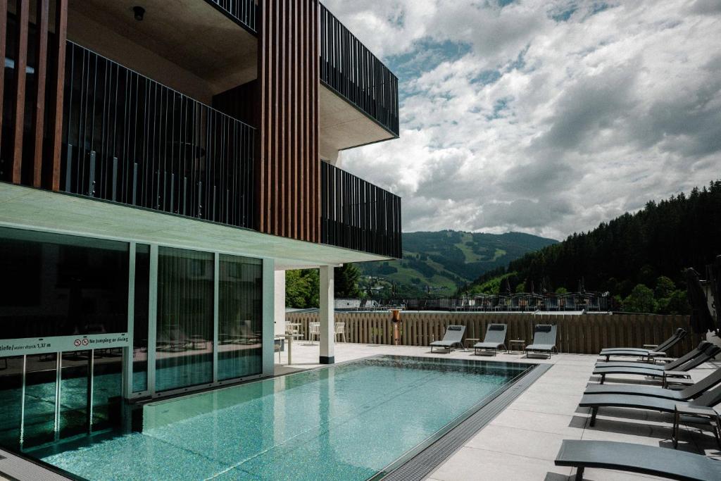 a building with a swimming pool and lounge chairs at LH Linzerhaus Suites Saalbach - inklusive Jokercard in Saalbach-Hinterglemm