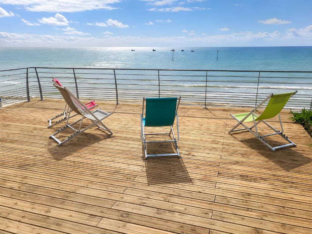 two chairs sitting on a deck looking at the ocean at L'hermitage, Villa Front De Mer in Pirou