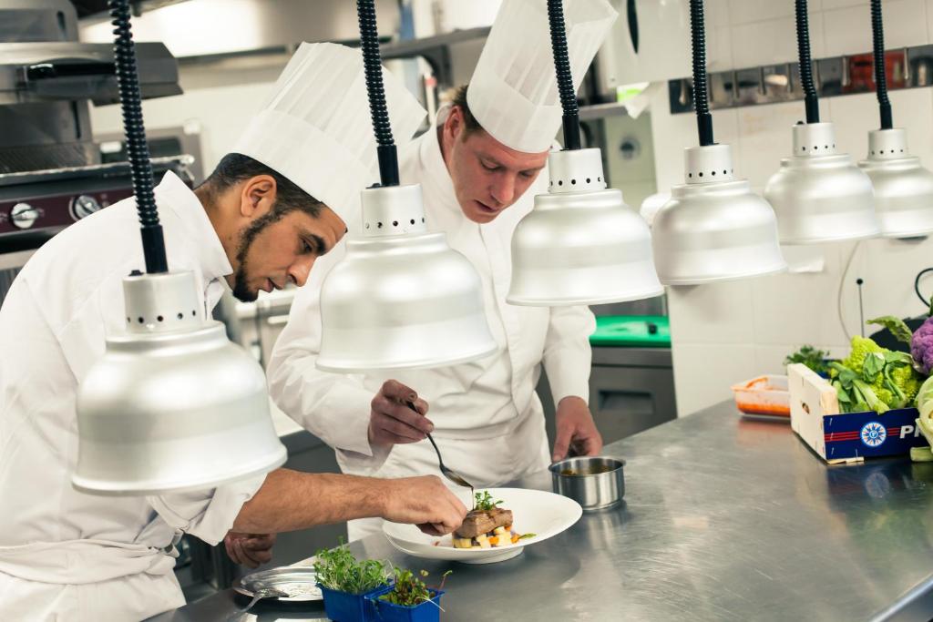 two chefs preparing a plate of food in a kitchen at Hôtel Taj-I Mah by Les Etincelles in Arc 2000