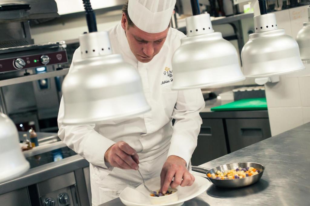 a chef preparing a plate of food in a kitchen at Hôtel Taj-I Mah by Les Etincelles in Arc 2000