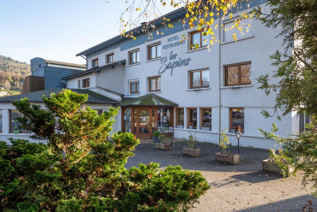 a large white building with trees in front of it at Logis Hotel les Sapins in Le Ménil