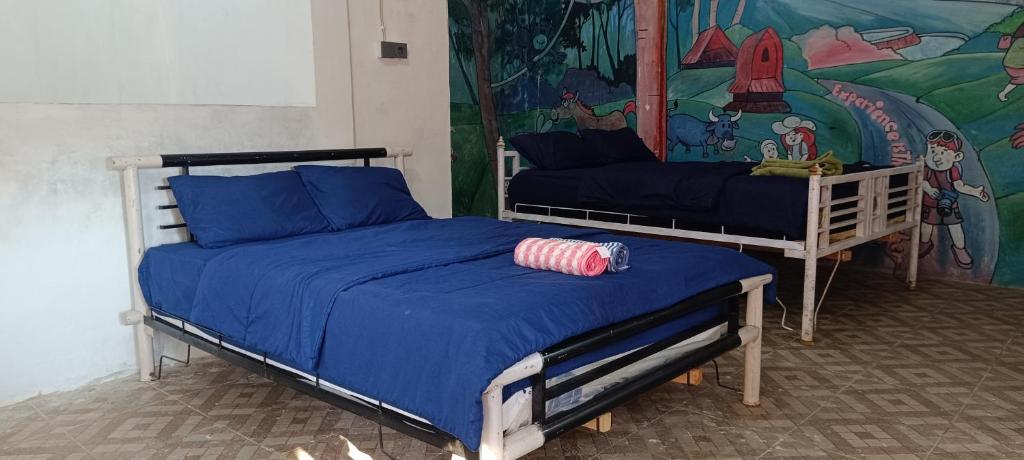 a bedroom with two beds with blue sheets and a mural at Hostel Tetebatu Terrace in Tetebatu