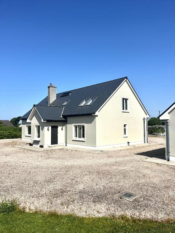 a white house with a black roof on a gravel driveway at Sioscadh na Mara in Spiddal