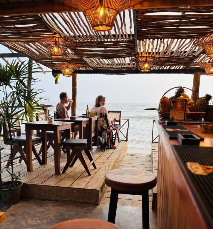 two people sitting at tables in a restaurant overlooking the ocean at Backpack Beach Hostel & Reggae Bar in Galle