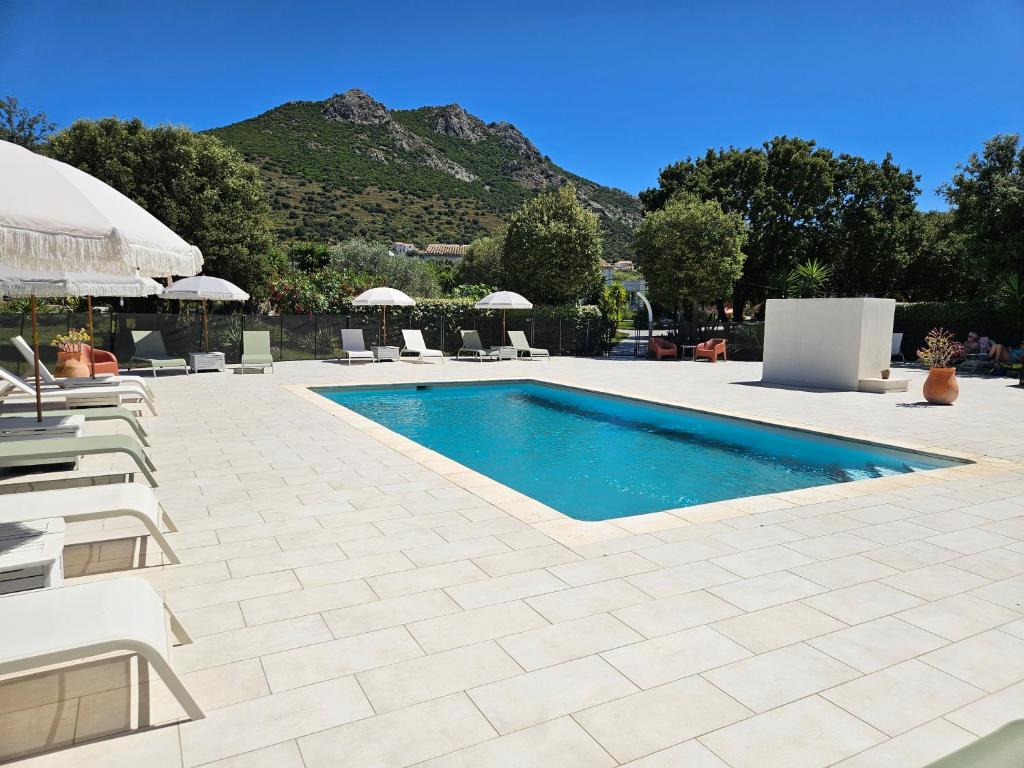 a swimming pool with chairs and a mountain in the background at Hôtel & Restaurant Les Mouettes in Belgodère