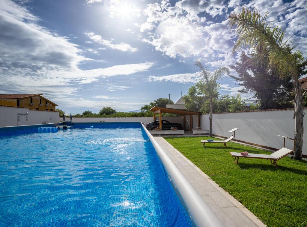 a large swimming pool with two chairs and a house at Villa Yasmine in Cinisi