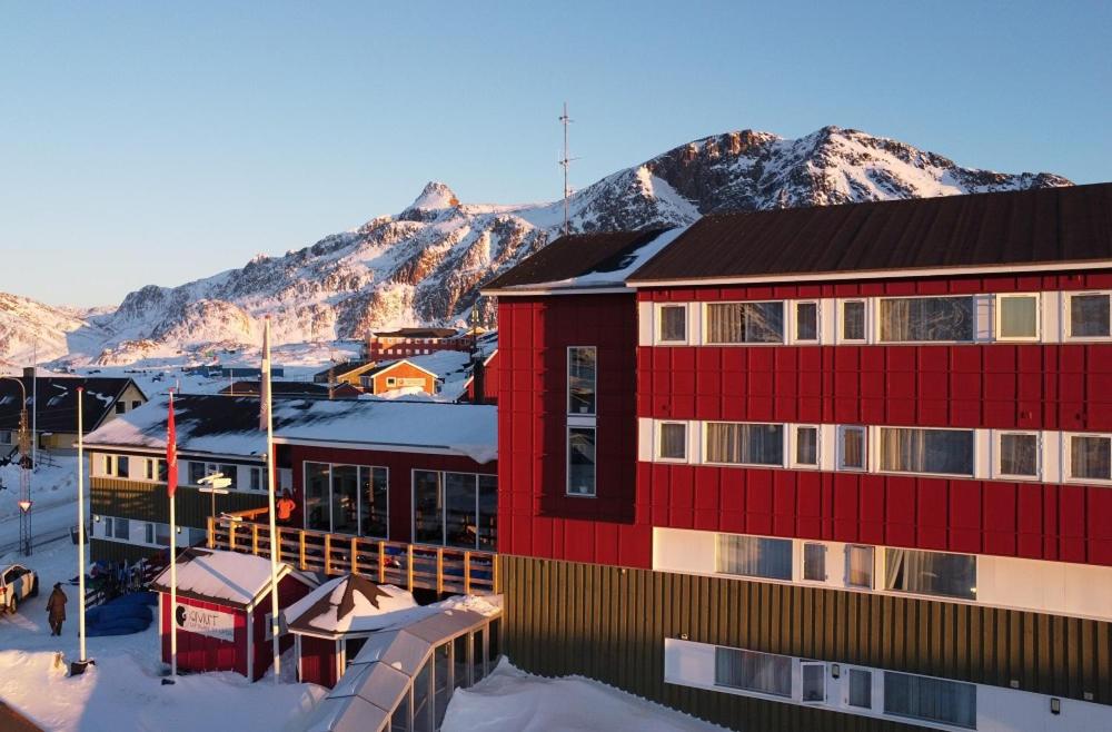 a red building with a mountain in the background at Backcountry Hotel Sisimiut in Sisimiut