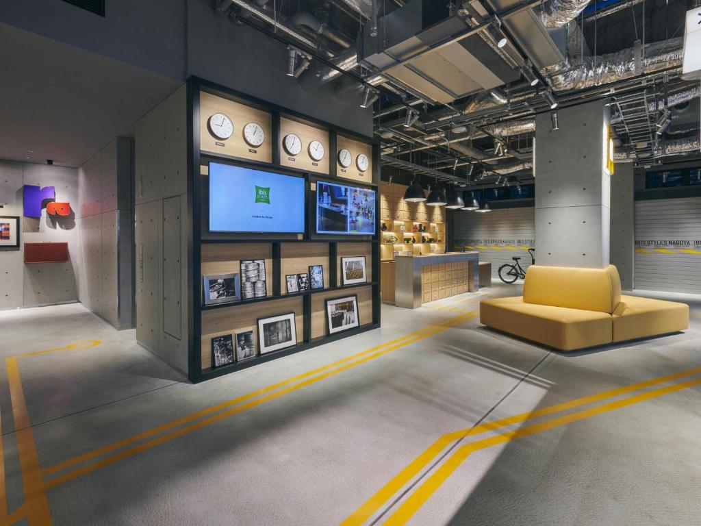 a room with a yellow couch and clocks on the wall at ibis Styles Nagoya in Nagoya