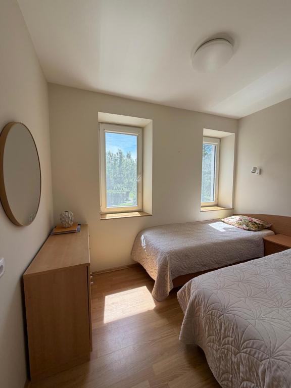 a bedroom with two beds and a mirror and two windows at Apartment Jūros Mėlis in Nida