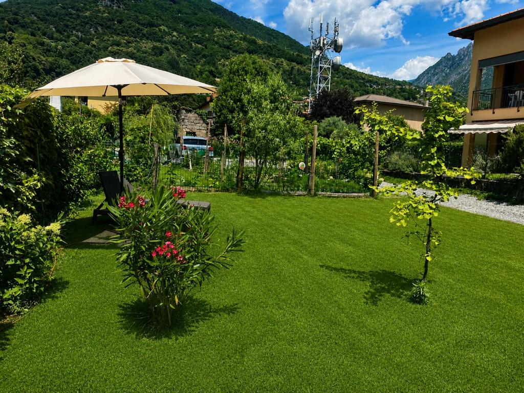 a lawn with an umbrella and flowers and a house at Lilly Garden Lago Lugano with private parking garden and air conditioning in Porlezza