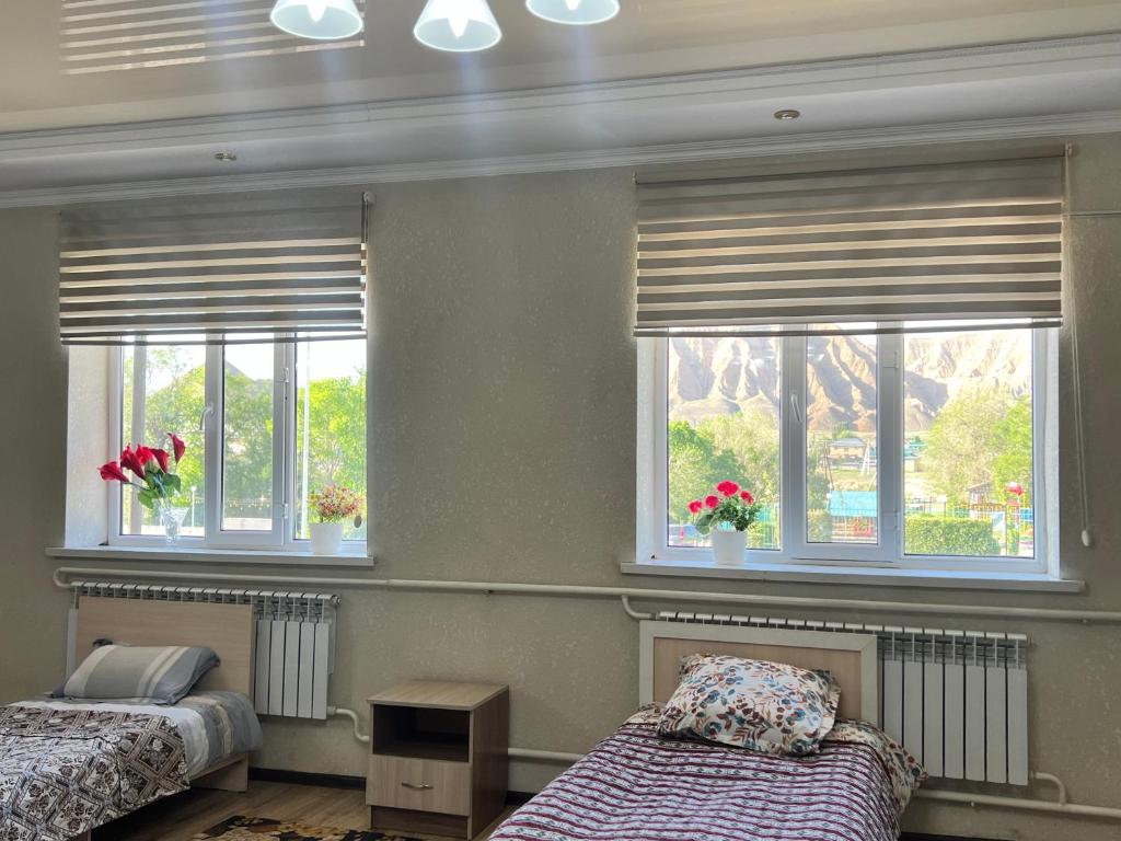 a bedroom with two beds and two windows with flowers at Apartmenthouse in Naryn