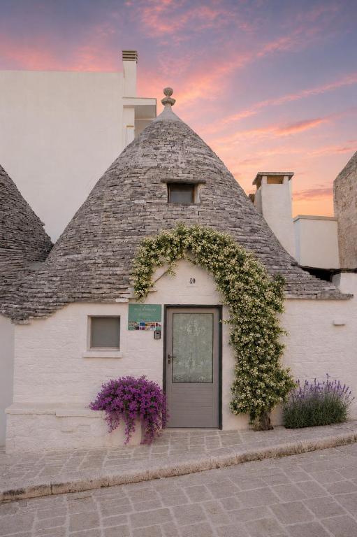 a white building with a roof with a door and flowers at Trullo Arboris in Alberobello