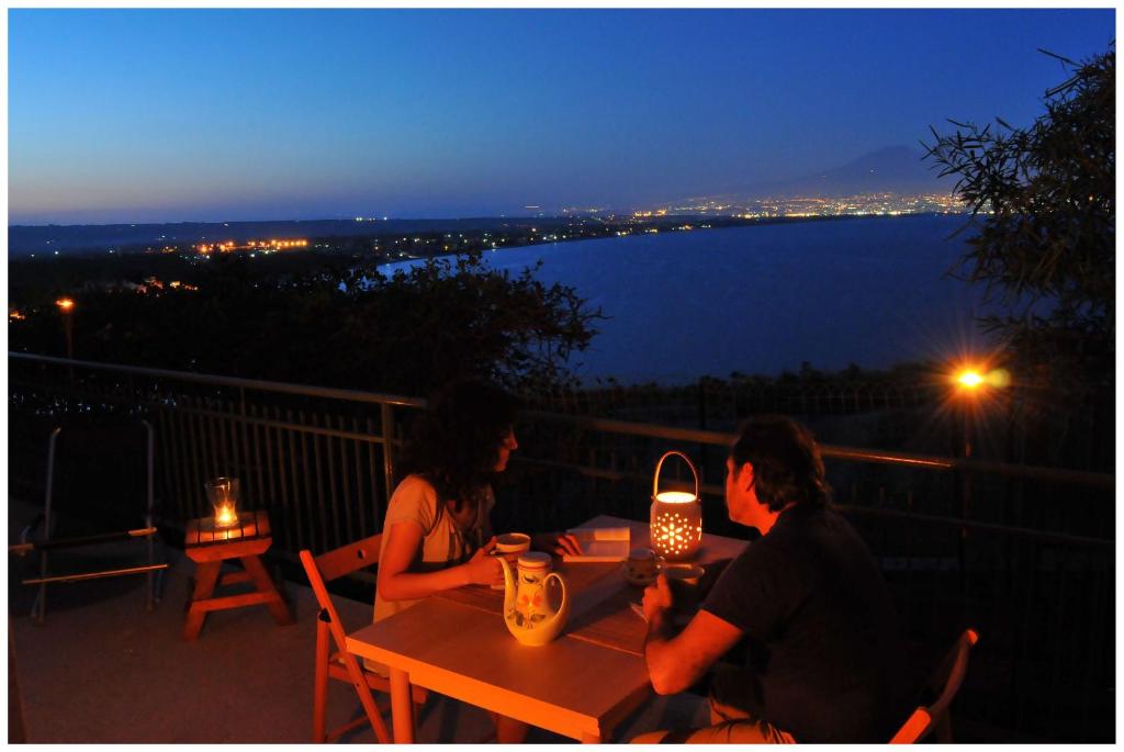 duas pessoas sentadas numa mesa numa varanda à noite em Villa Margiu - Casa Ossino em Agnone Bagni