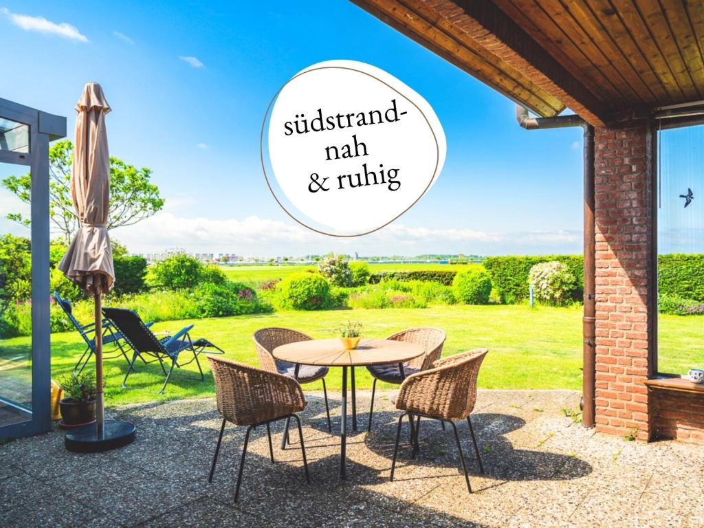 a patio with a table and chairs with a view of a field at Huus Binnensee - Erdgeschoss-Wohnung mit Garten & Seeblick - Wintergarten & Terrasse - hundefreundlich - ruhige Lage - Südstrand 5 Min mit Rad in Fehmarn