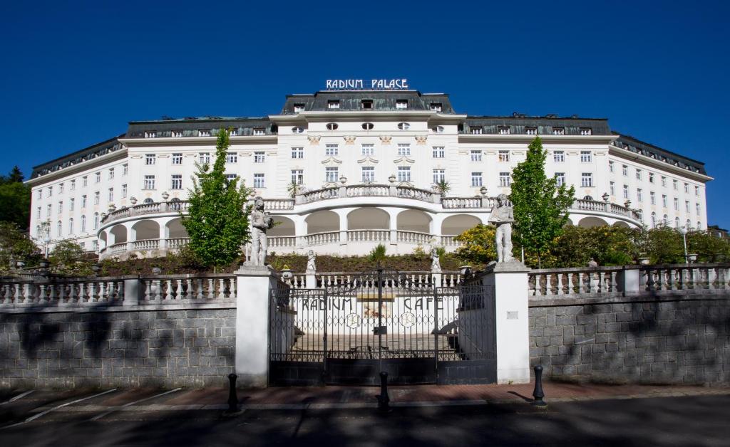 a white building with a fence in front of it at Hotel Radium Palace in Jáchymov