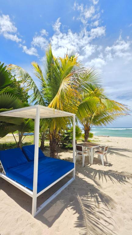 a bed and a table on a beach with palm trees at El Tridente in Juan Dolio