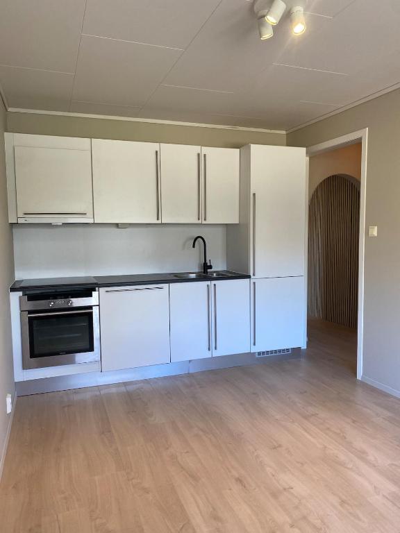 an empty kitchen with white cabinets and a sink at Appartment in Jørpeland