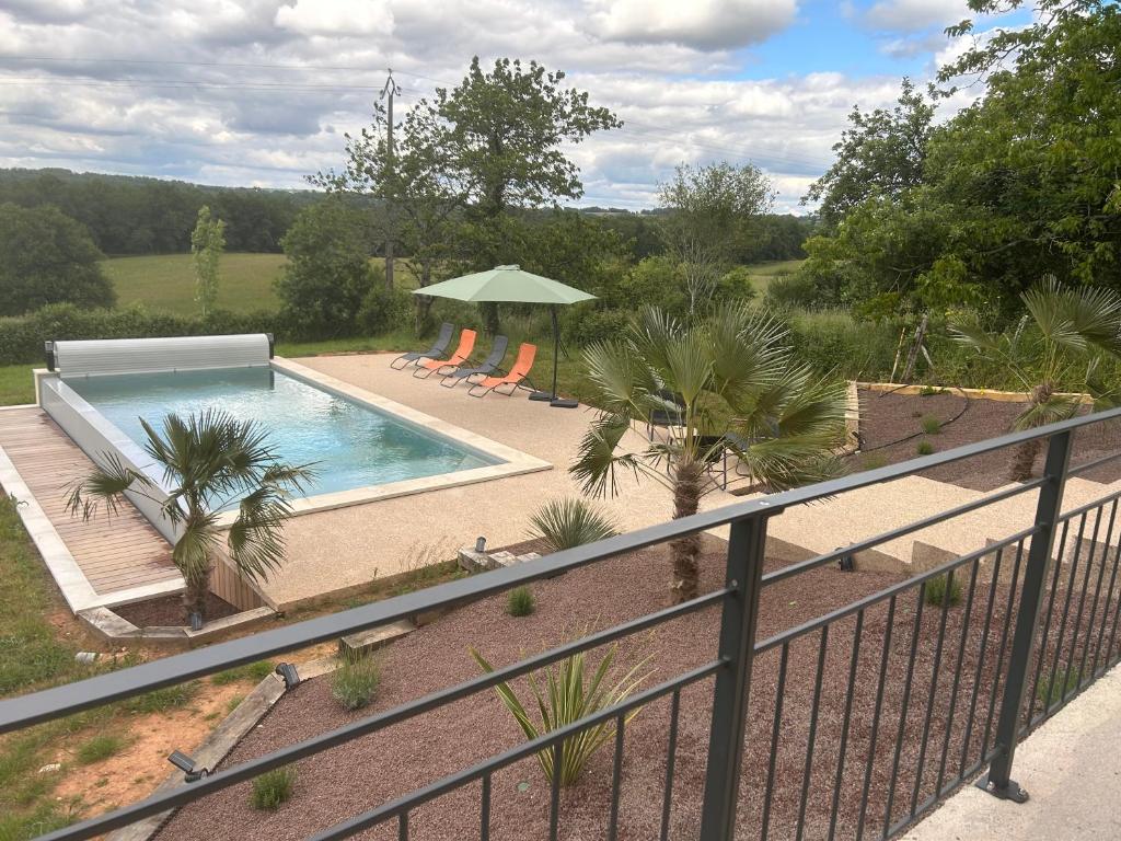 a swimming pool with chairs and a green umbrella at Gîte Les Jacquets in Hautefort