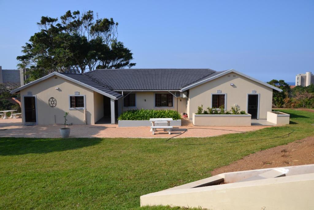 a white house with a bench in a yard at Sea & Forest Self Catering Estate - Durban Kingsburgh in Kingsborough