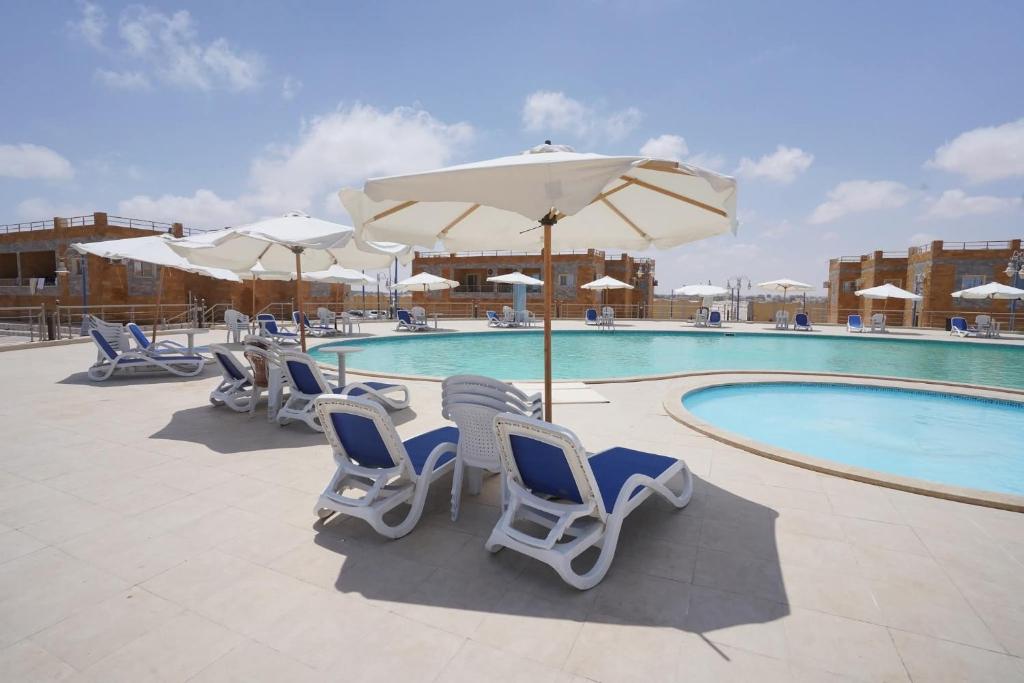 a group of chairs and umbrellas next to a swimming pool at Ghazala resort in Marsa Matruh