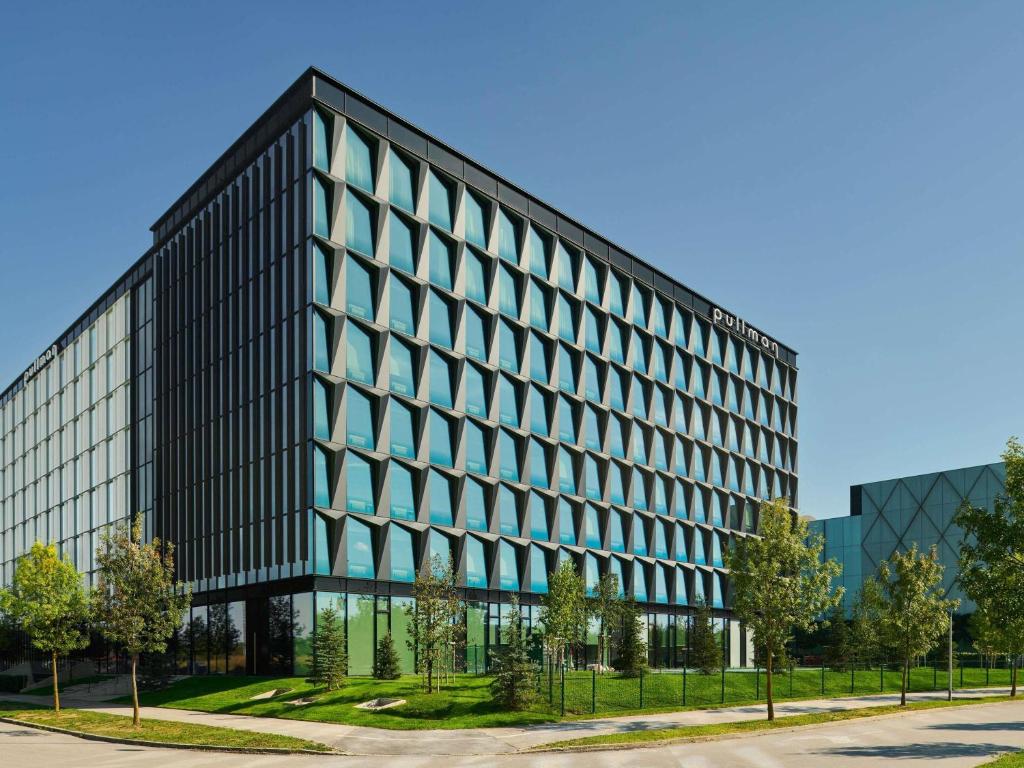Glass-clad office building with stepped diamond-shaped windows and 'Pullman' sign, landscaped lawn and paved walkway at Pullman Zagreb in Zagreb