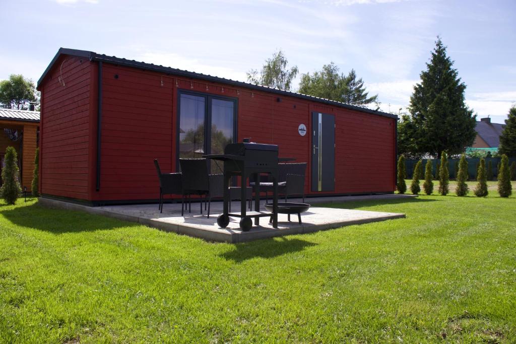 a red shed with a table and chairs in a yard at By The Lake - Domki I Sauna Nad Jeziorem in Załęże