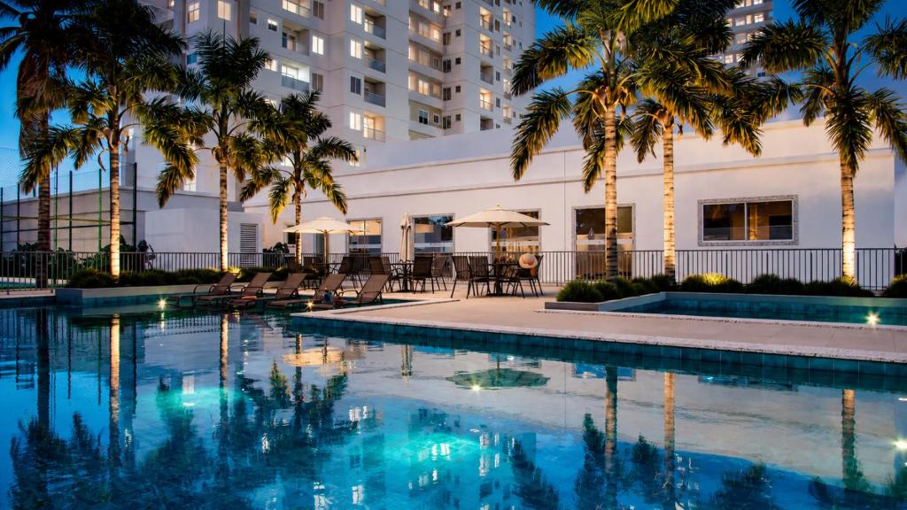 a pool with palm trees in front of a building at Apartamento completo em Ponta de Campina, 2 quartos, piscina, academia e Wi-Fi in Cabedelo