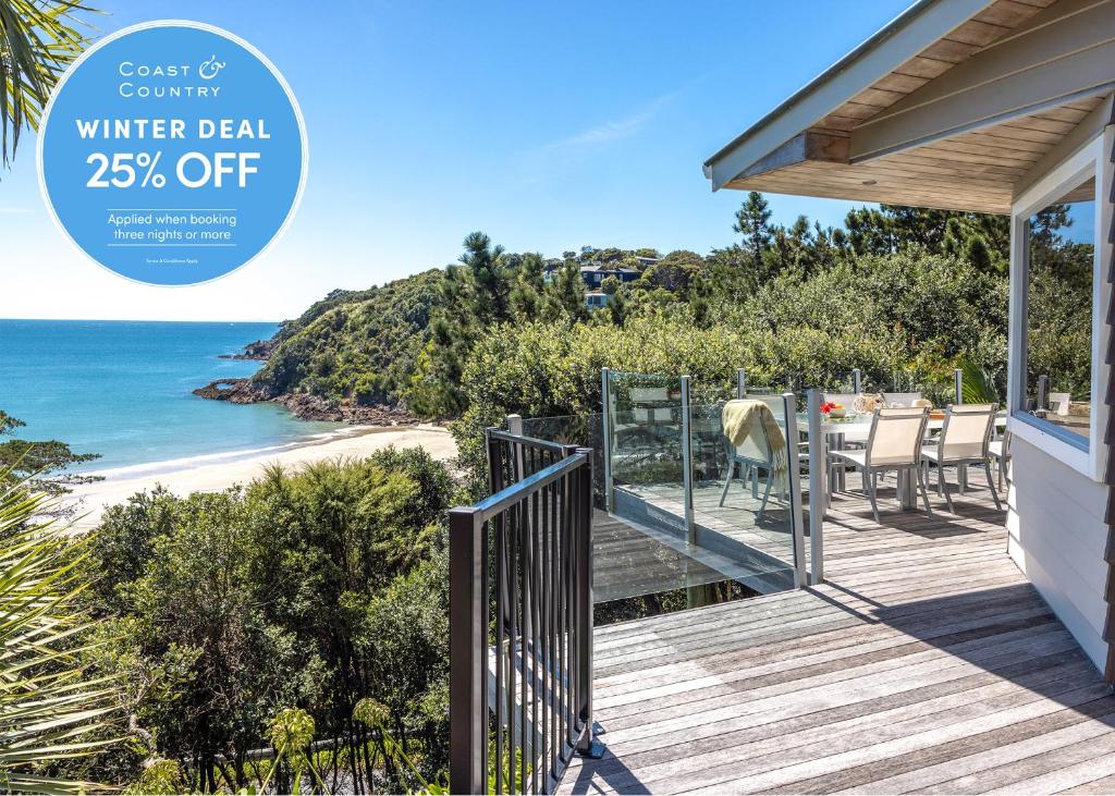 a house with a deck with a view of the beach at Tawa Cottage - Coast & Country in Oneroa