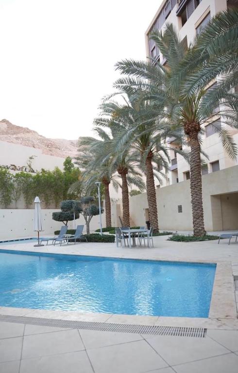a swimming pool with palm trees next to a building at aura alraha village in Aqaba
