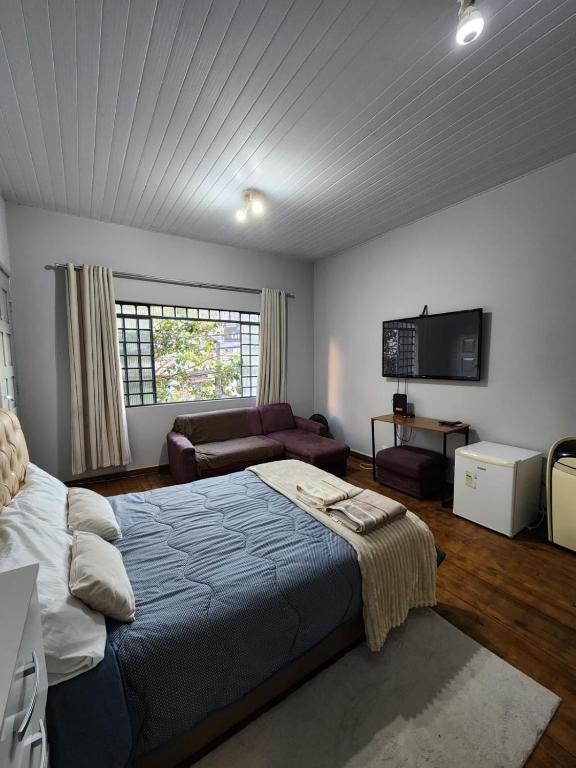 a bedroom with a bed and a couch and a television at Quarto no coracao da cidade entre batel, merces e centro Excelente localizacao in Curitiba