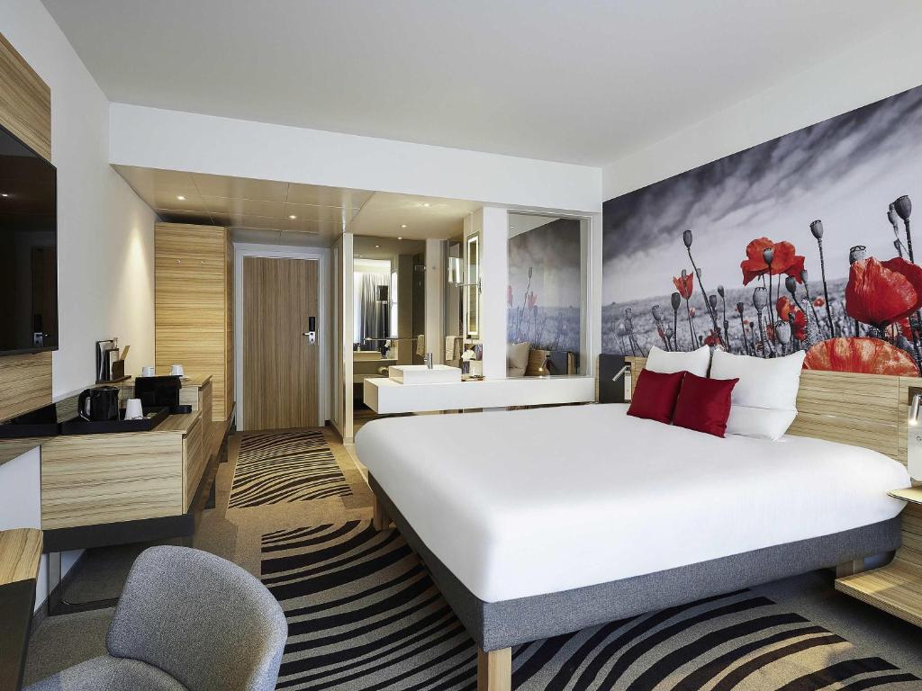 a hotel room with a large bed and a bathroom at Novotel Ieper Centrum in Ieper