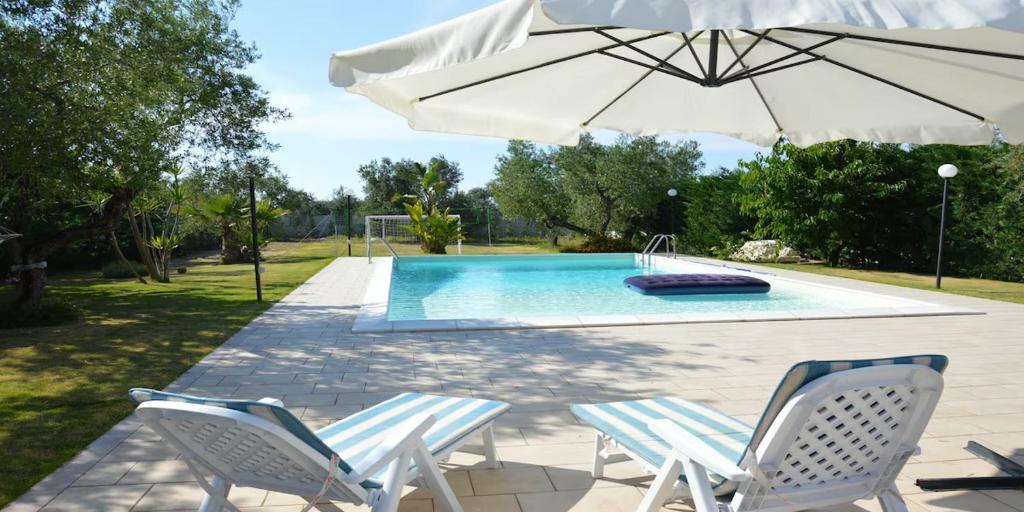 a swimming pool with two chairs and an umbrella at Villa MEMA in Bisceglie