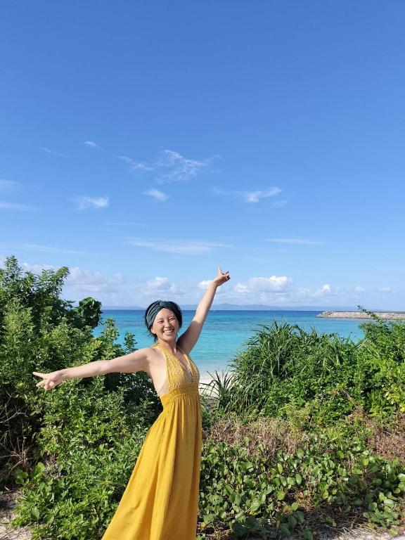 a woman in a yellow dress standing in front of the ocean at Holistic retreat Coco in Ishigaki Island