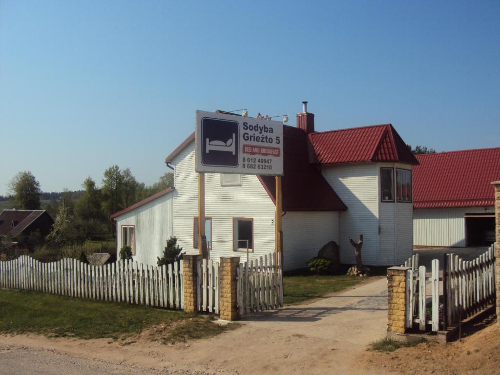 un panneau devant une maison blanche avec une clôture dans l'établissement Griežto 5, à Zarasai