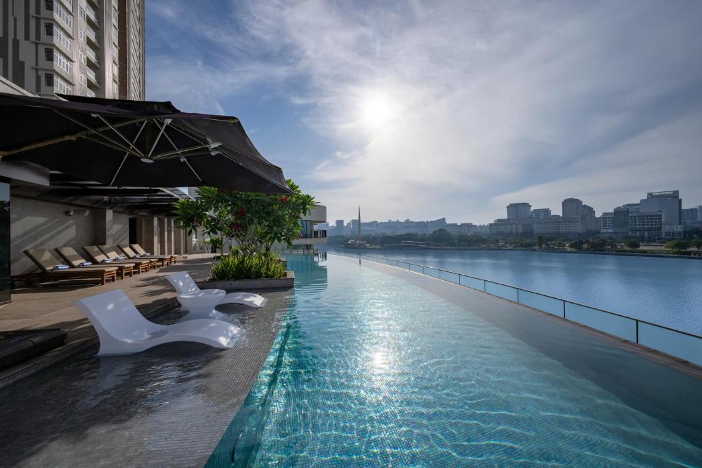 a swimming pool with white chairs and a body of water at Fraser Residence Putrajaya in Putrajaya