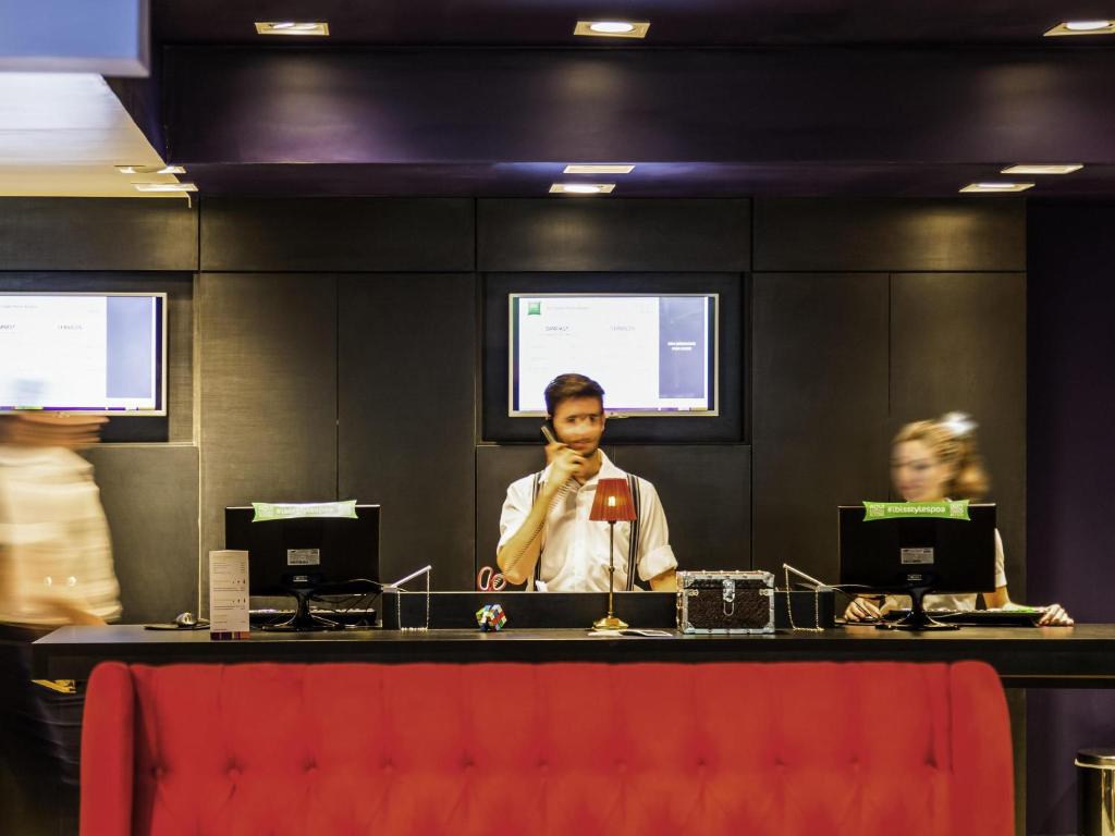 a man standing behind a counter with a red chair at Ibis Styles Porto Alegre Centro - proximo rodoviaria, Araujo Vianna e hospitais in Porto Alegre