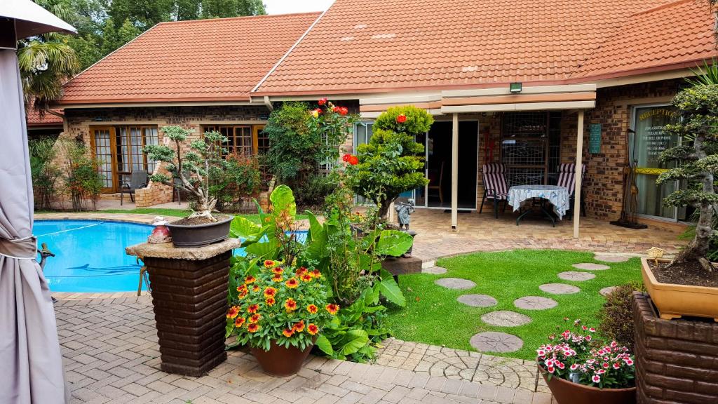 a house with a garden with flowers and a pool at Aark Guest Lodge in Vanderbijlpark