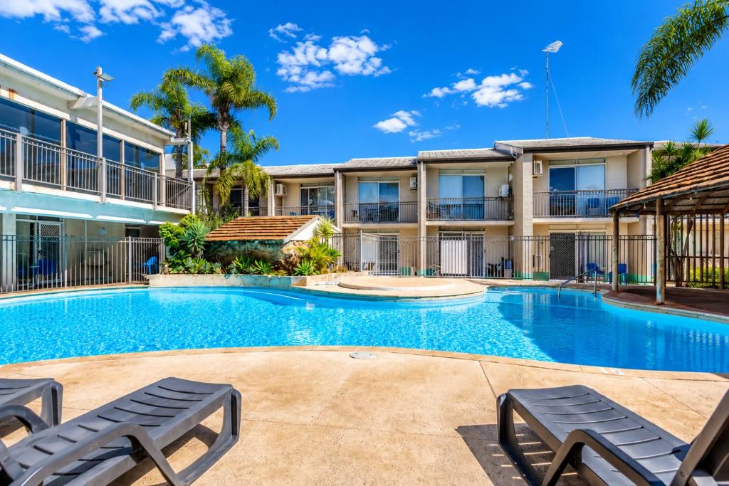 a swimming pool with two lounge chairs in front of a building at Sea Breeze Apartment in Mandurah