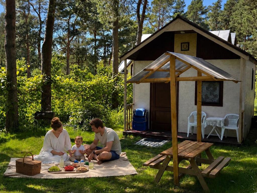 a family sitting on a picnic blanket in front of a cabin at Zem Priedēm in Lapmežciems