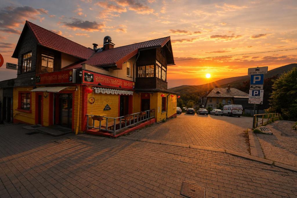 a building on a street with the sunset in the background at Apartamenty i Pokoje w centrum Karpacza in Karpacz