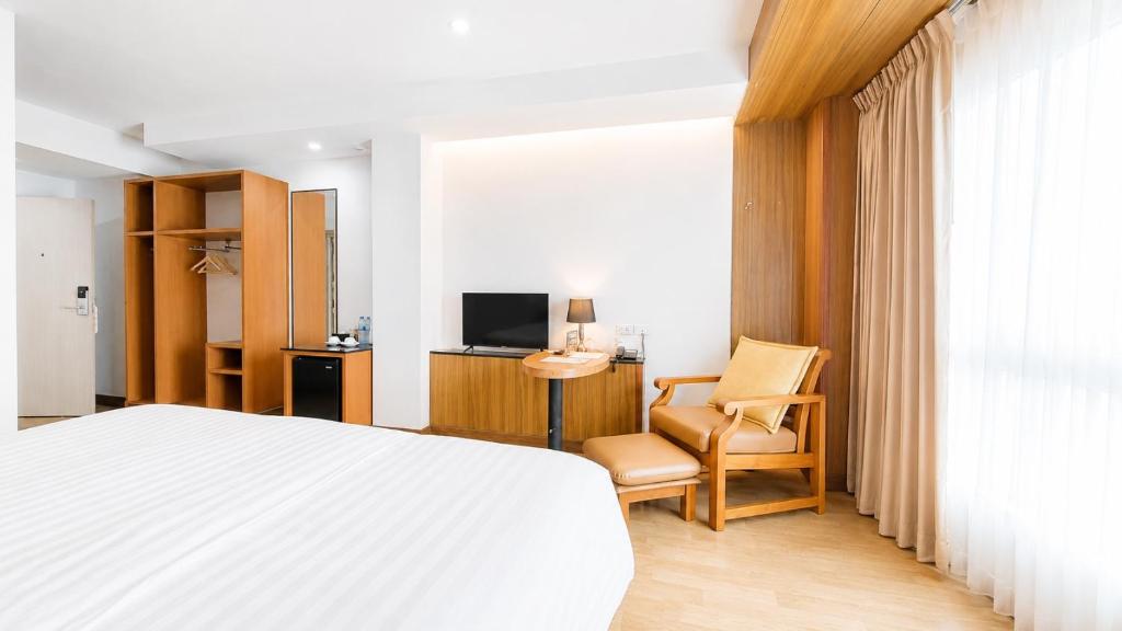 A room with a large bed, lounge chair, television and open wardrobe storage.