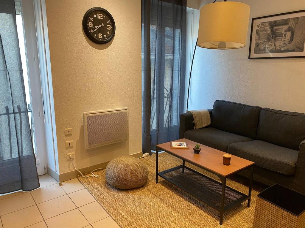 a living room with a couch and a table and a clock at Dax Fontaine Chaude Center in Dax