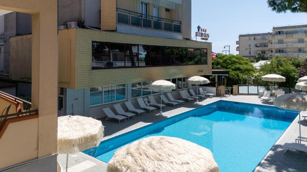 a swimming pool in front of a building with chairs and umbrellas at Hotel Simon in Gatteo a Mare