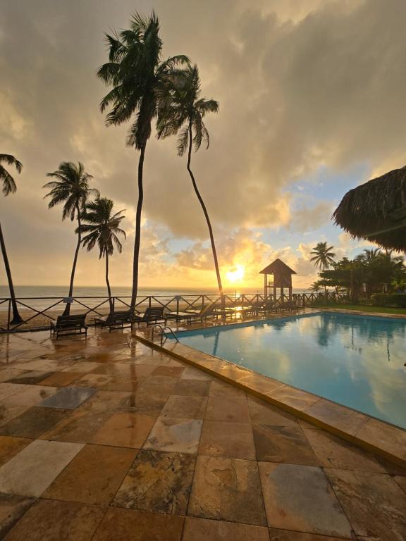 a pool with palm trees and the ocean at sunset at Eco Paradise 129 in Caucaia