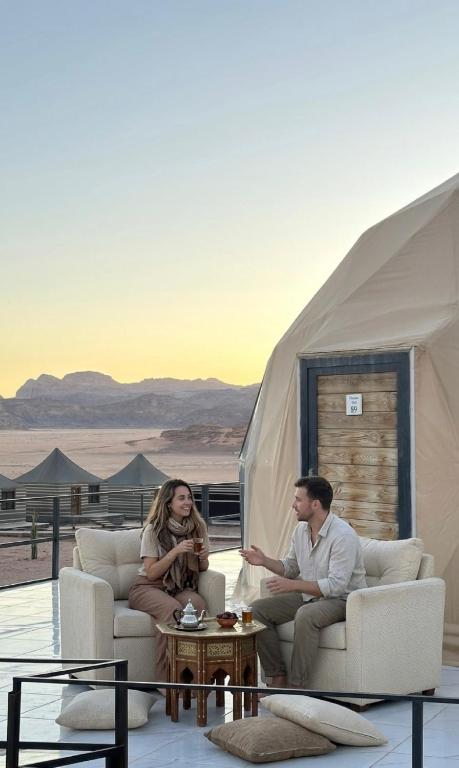 a man and woman sitting in chairs in a tent at WADI RUM NASA lUXURY BUBBLE in Wadi Rum
