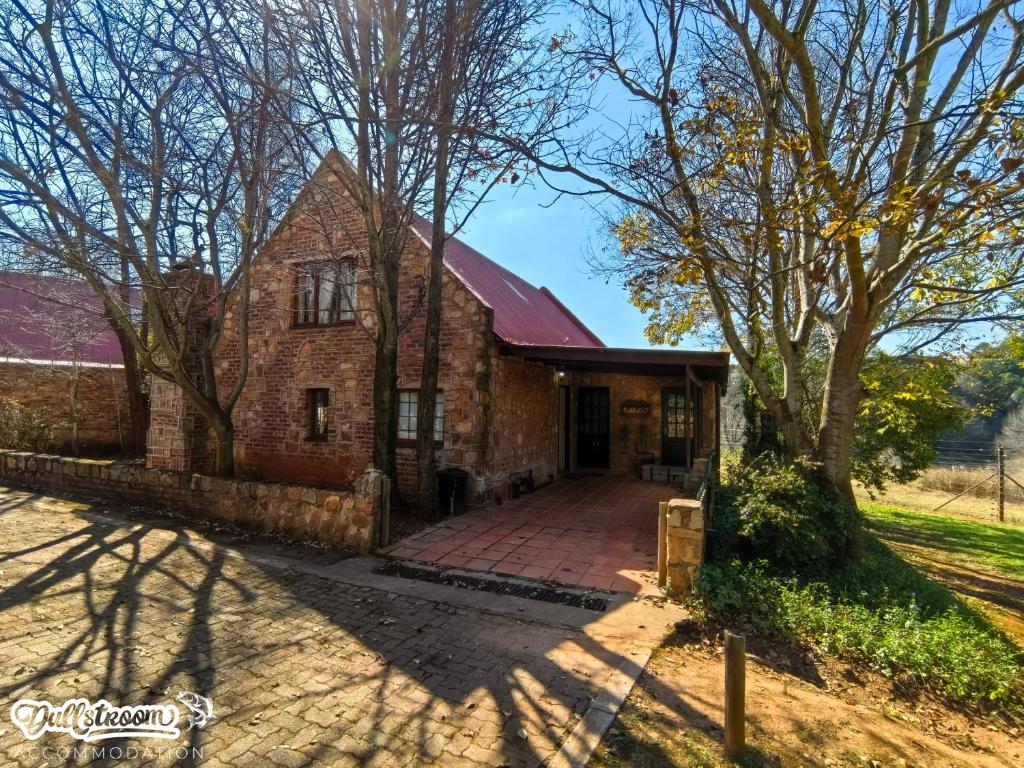 an old brick house with a driveway and trees at Critchley Common in Dullstroom
