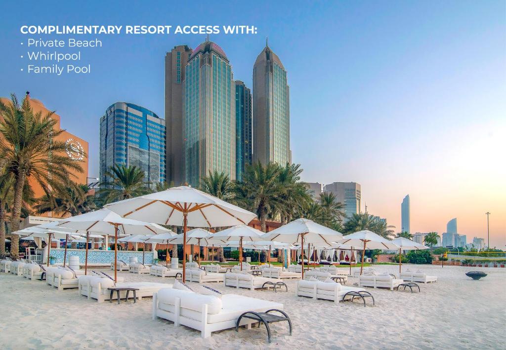 a beach with white chairs and umbrellas in front of a city at Sheraton Abu Dhabi Hotel & Resort in Abu Dhabi