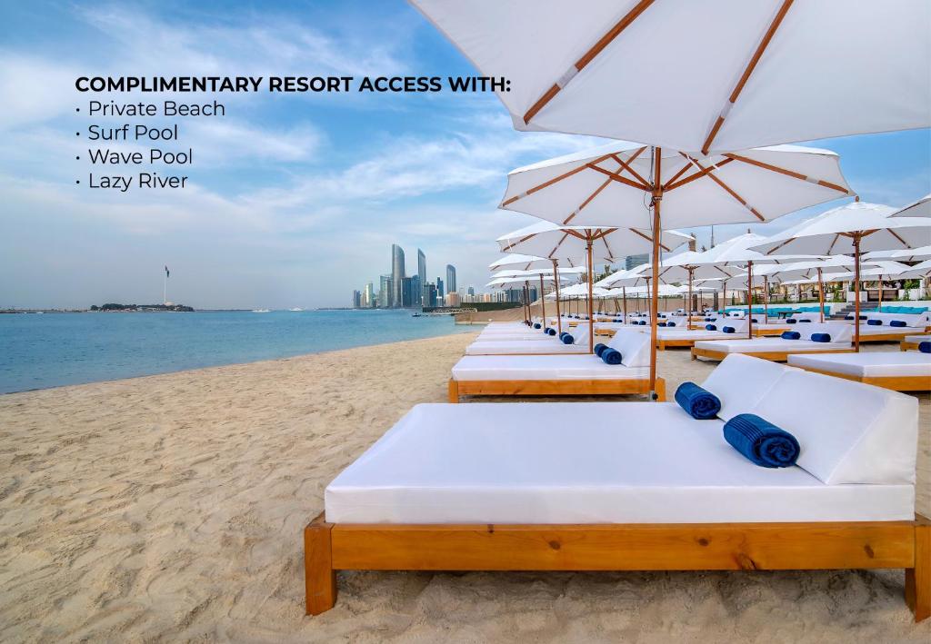 a row of beds on a beach with umbrellas at Radisson Blu Hotel & Resort, Abu Dhabi Corniche in Abu Dhabi